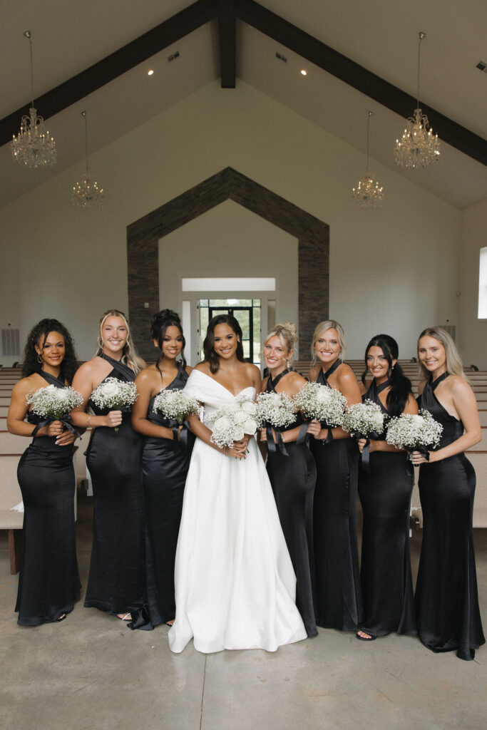 the bride with her bridesmaids, bridesmaids are wearing all black and they are all holding white flower bouquets