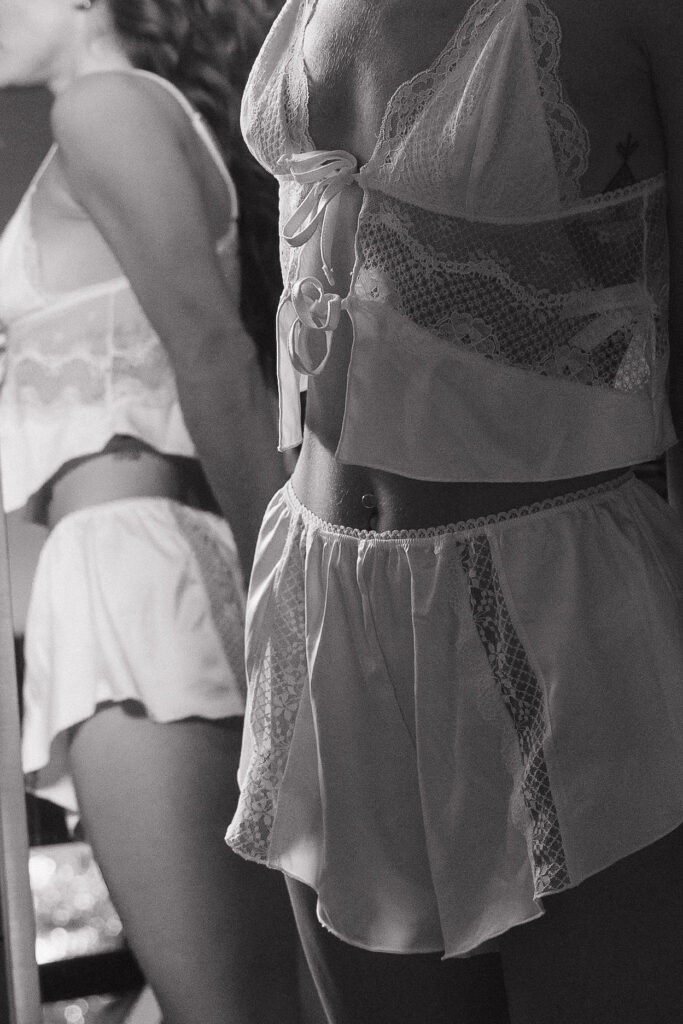 A moody black-and-white shot of the bride and another person in delicate lace lingerie, highlighting intricate details and textures in a stylish and intimate setting.