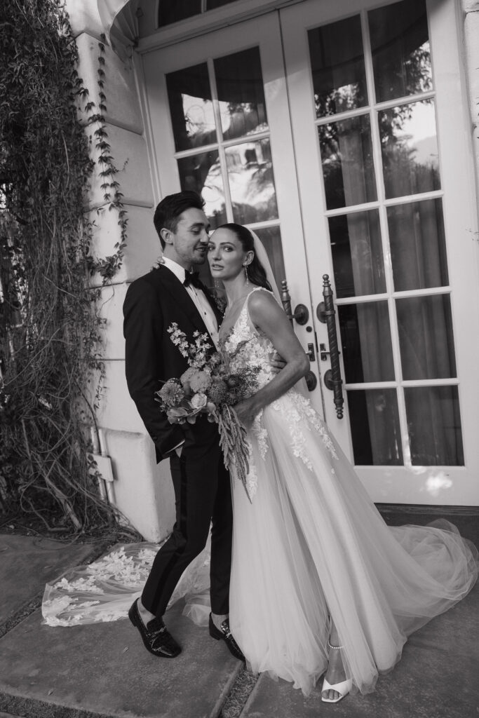 A black-and-white portrait of the bride and groom leaning close to each other outside a door framed with ivy at Park Palm Springs Hotel, evoking a timeless and intimate moment.