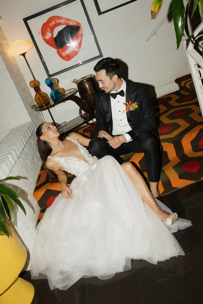 The bride and groom seated on a patterned floor, sharing a quiet moment together under colorful artwork and lighting.