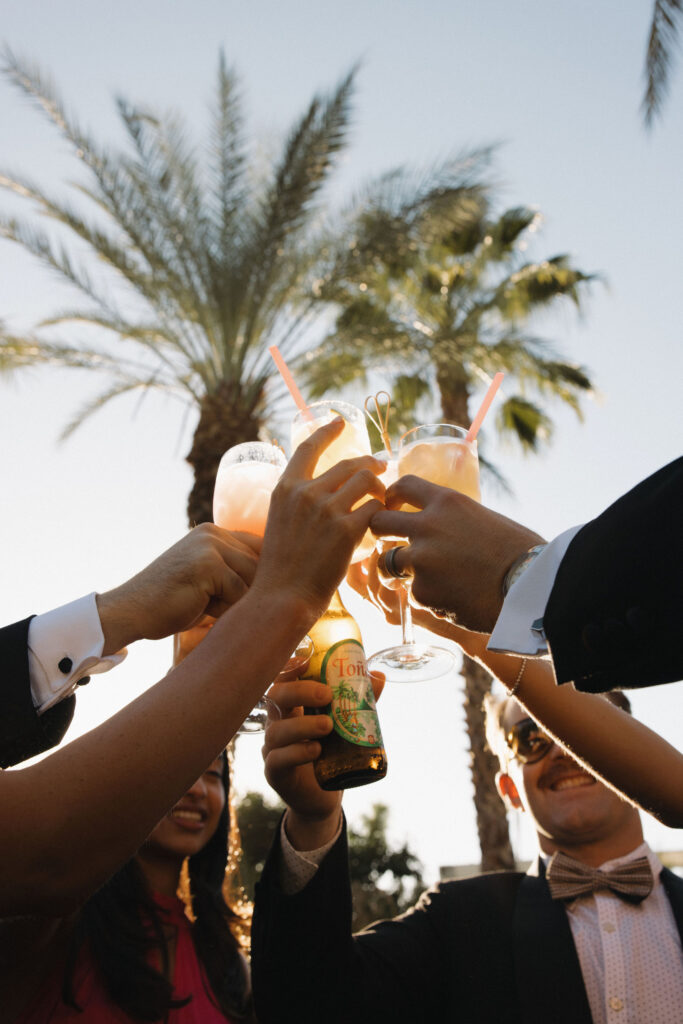 Daytime toast with cocktails and palm trees in the background - A group of people clinks glasses filled with cocktails against a backdrop of palm trees, enjoying a sunny day celebration.