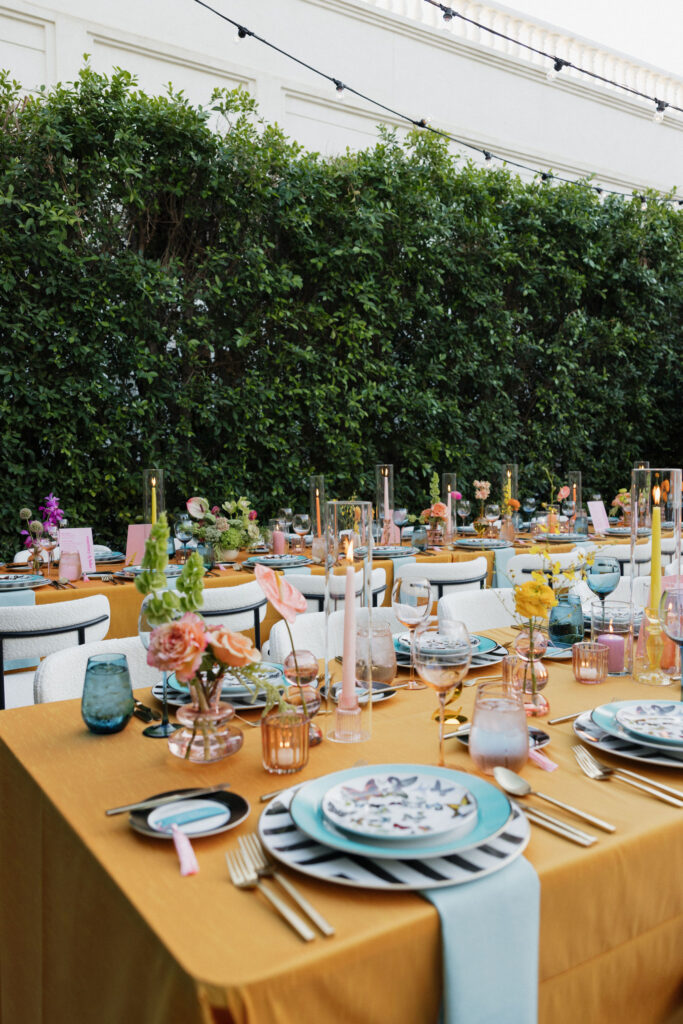 Rows of beautifully decorated tables with orange tablecloths, colorful glassware, and vibrant floral centerpieces, under a canopy with hanging disco balls and fringed lanterns at Park Palm Springs Hotel.