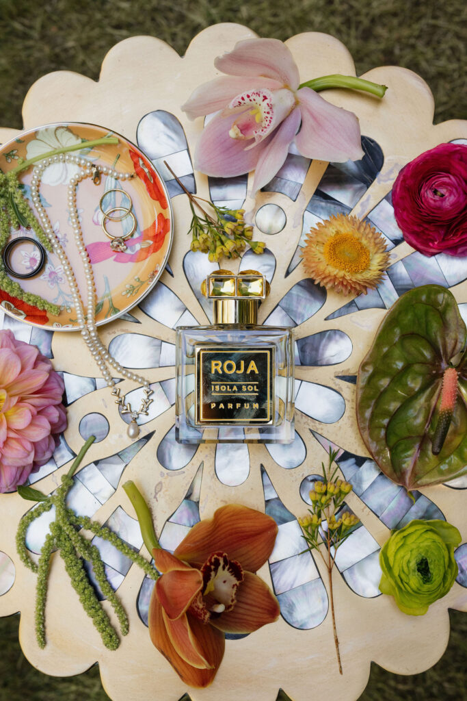 A perfume bottle and jewelry surrounded by vibrant flowers arranged on a decorative table.