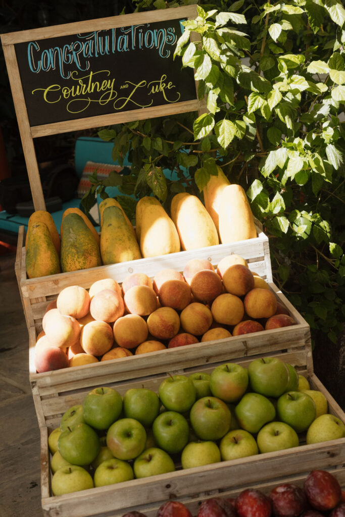 A rustic display of fresh fruit in wooden crates, with a sign that reads “Congratulations Courtney and Luke” above it.