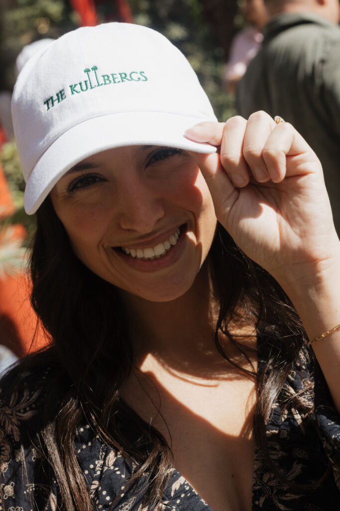 Close-up of a smiling guest in a white baseball cap - A guest smiles warmly at the camera, wearing a white cap embroidered with “The Kullbergs.”