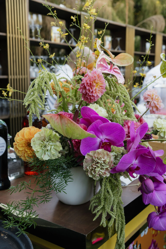 A vibrant floral arrangement with pink orchids, dahlias, and greenery adds a pop of color to the bar setup at Park Palm Springs Hotel.