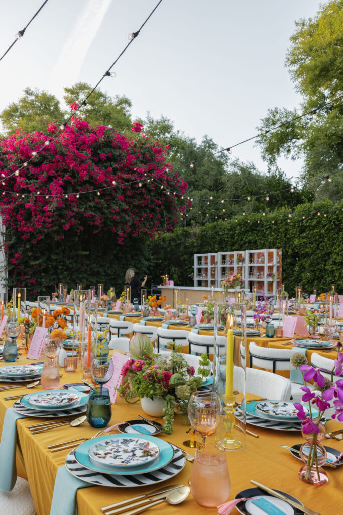 Rows of beautifully decorated tables with orange tablecloths, colorful glassware, and vibrant floral centerpieces, under a canopy with hanging disco balls and fringed lanterns at Park Palm Springs Hotel.