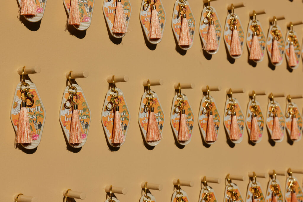 Unique keychain wedding favors with colorful tassels and vibrant designs hang on a beige wall at Park Palm Springs Hotel, adding a personal and playful touch to the celebration.