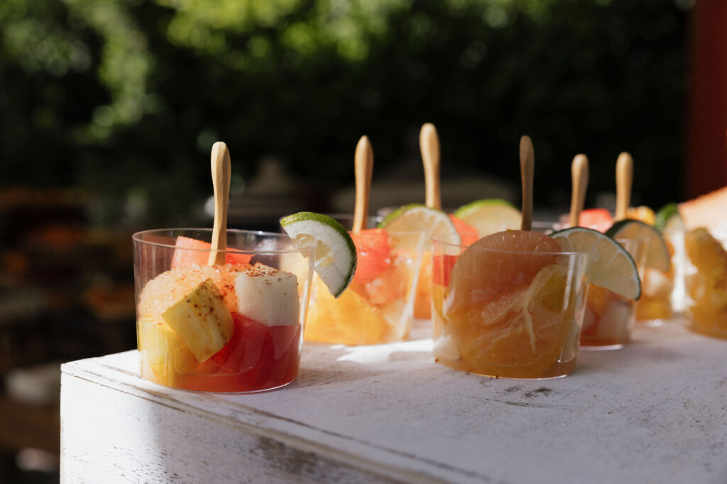 Fruit cups with wooden spoons - Small cups filled with colorful fruit and garnished with lime wedges, neatly arranged and ready to be served to guests.