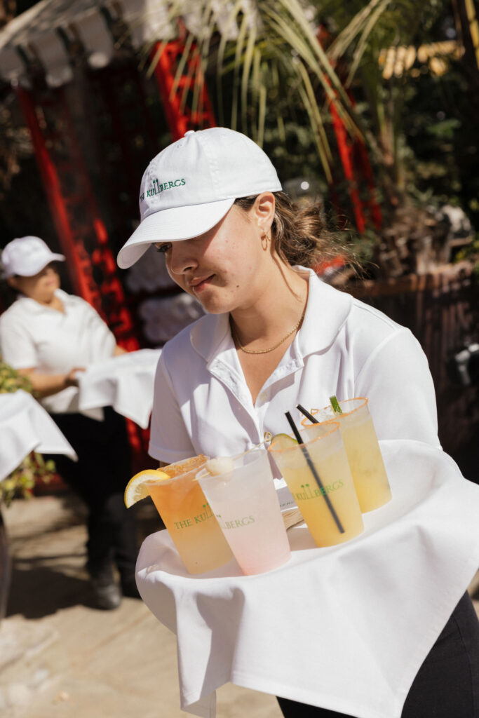 A server at Park Palm Springs Hotel carries a tray of cocktails garnished with citrus slices and served in cups labeled “The Kullbergs.”