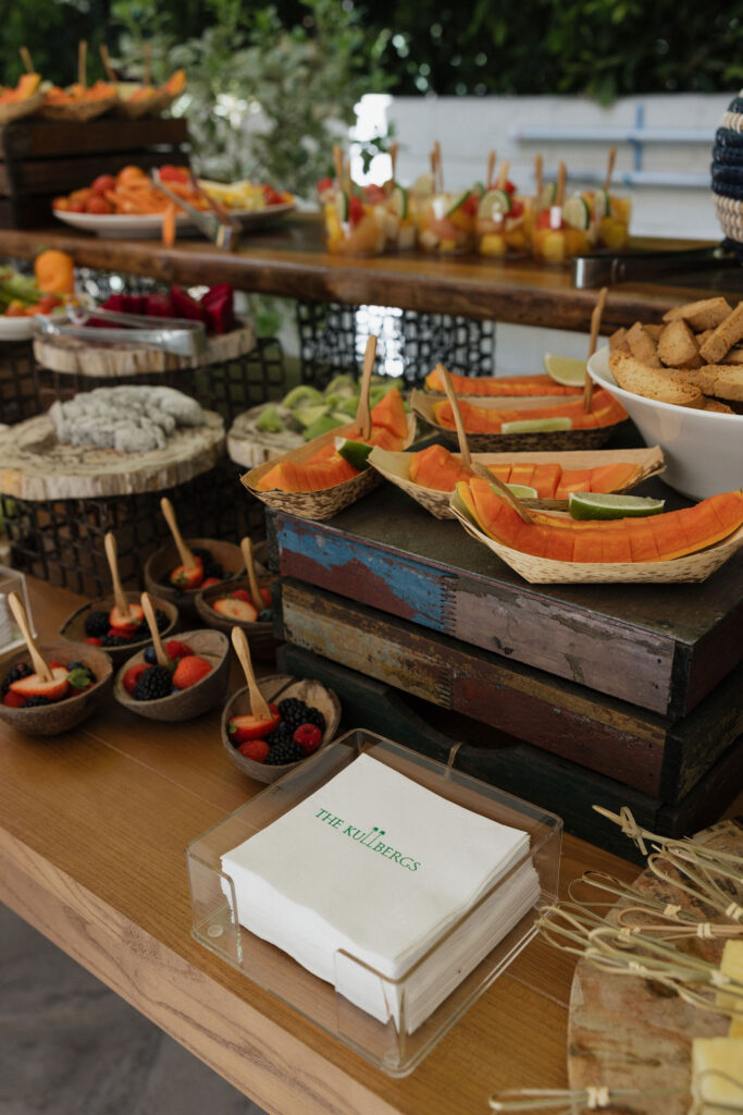 A rustic display of fresh fruits and desserts with "The Kullbergs" personalized napkins at Park Palm Springs Hotel, creating a welcoming snack setup for guests.