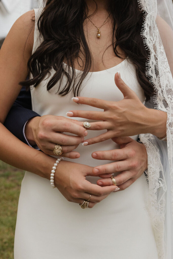 Close-up of the bride's hands with wedding rings on display, embraced by the groom's hands, capturing intricate jewelry details.