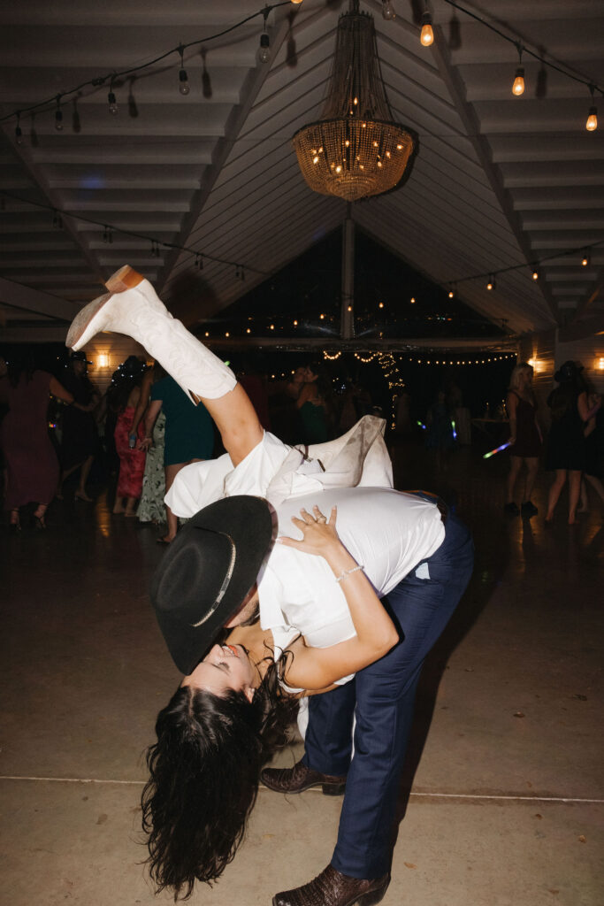 The bride and groom share an energetic dance during the reception, showcasing joy and movement against the backdrop of string lights.