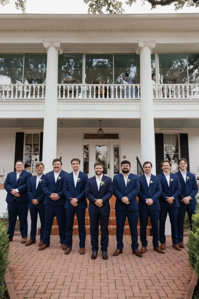 The groom and his groomsmen line up on the front steps of the inn, dressed in matching navy suits and boutonnieres, with the inn's iconic white pillars as the backdrop.