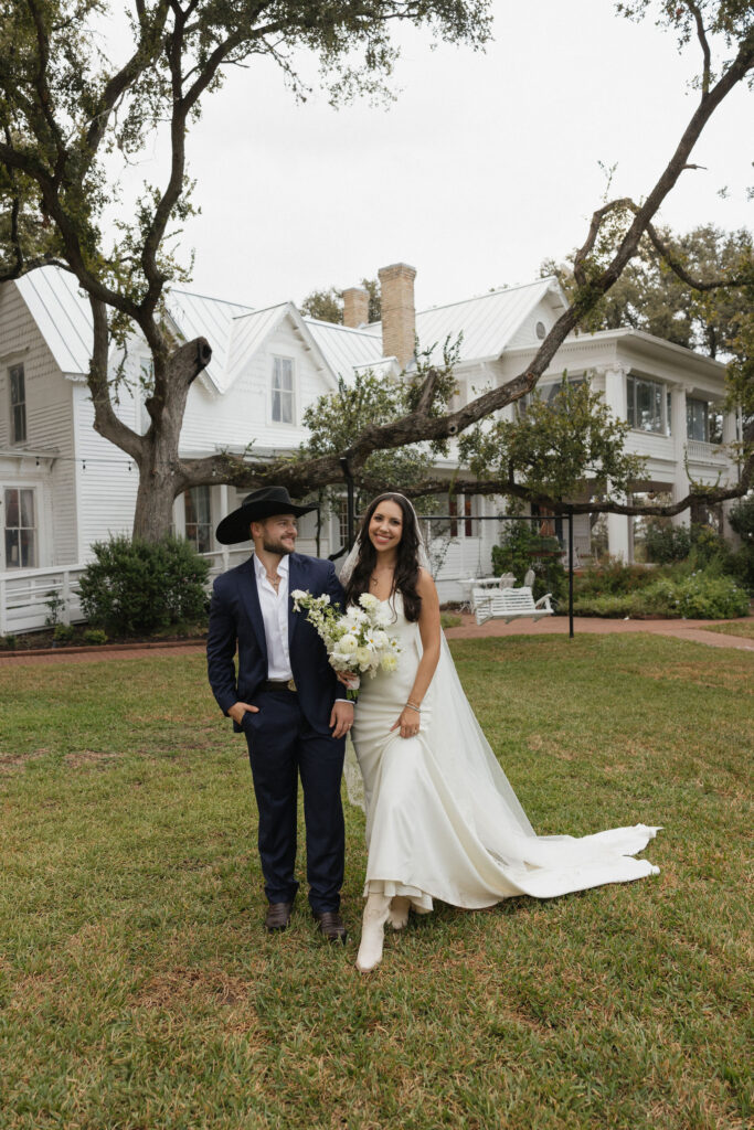 The bride and groom stand in front of The Winfield Inn’s picturesque exterior, surrounded by green lawns and rustic charm.