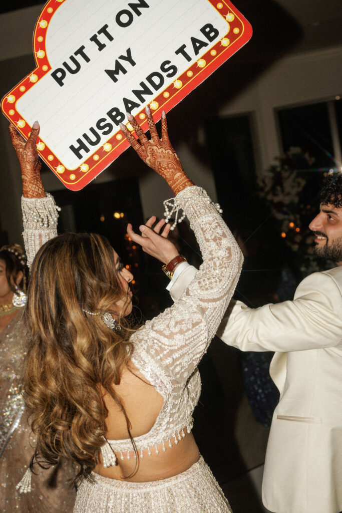 A bride holding up a sign that says put it on my husbands tab