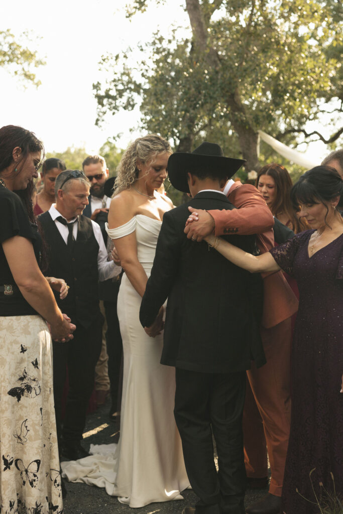 family praying over the bride and groom