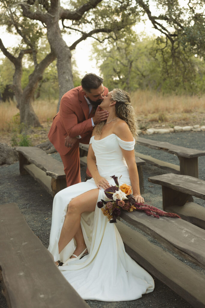 bride and groom kiss on bench at the cedars ranch